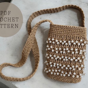 Może przedstawiać: Torebka wykonana na szydełku z długim paskiem i białymi koralikami. Torebka jest wykonana z naturalnego włókna i ma rustykalny wygląd. Obraz zawiera tekst "PDF CROCHET PATTERN".