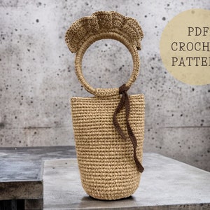 May include: A crochet bag with a brown handle and a ruffled top. The bag is made of a natural fiber and has a light brown color. The bag is sitting on a gray surface. PDF CROCHET PATTERN.