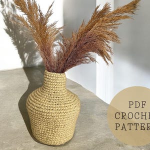 Könnte beinhalten: Eine gehäkelte Vase aus Naturfaser, in hellbrauner Farbe, mit runder, bauchiger Form. Die Vase ist mit getrocknetem Pampasgras gefüllt. Der Text "PDF CROCHET PATTERN" ist in der unteren rechten Ecke des Bildes sichtbar.