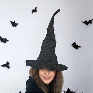 May include: A black witch hat with a tall, pointed crown and a wide brim. The hat is made of crocheted fabric and has a textured surface.