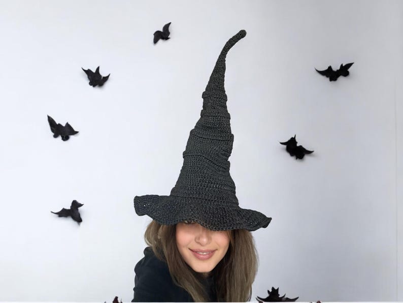 May include: A black witch hat with a tall, pointed crown and a wide brim. The hat is made of crocheted fabric and has a textured surface.