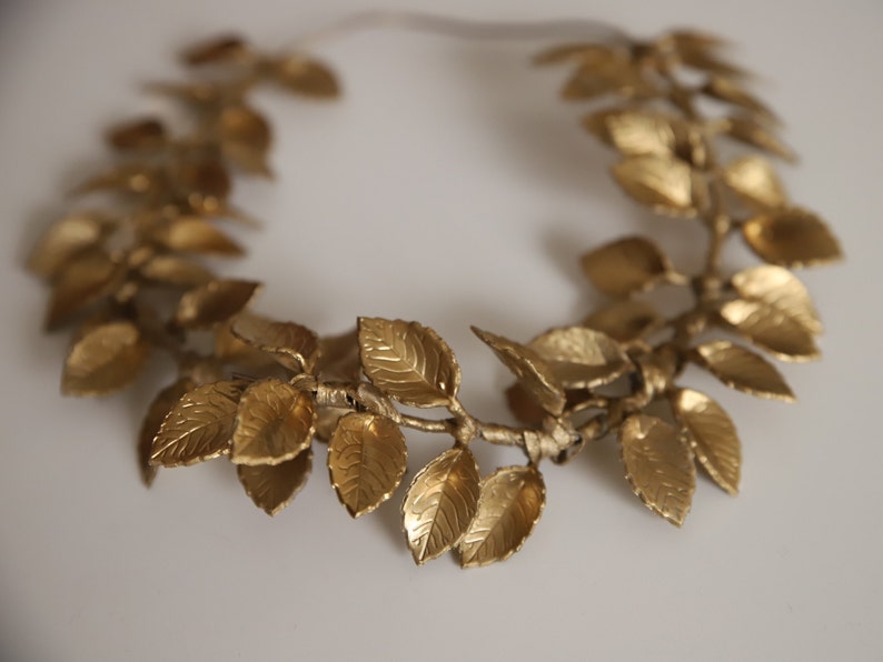 Może przedstawiać: Złota korona z liści o prostym wzorze. Korona wykonana jest z pojedynczych liści połączonych ze sobą w okrąg.