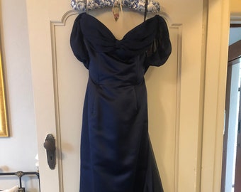 May include: A navy blue off-the-shoulder gown with a fitted bodice and a flowing skirt. The skirt has a ruffled detail at the bottom.