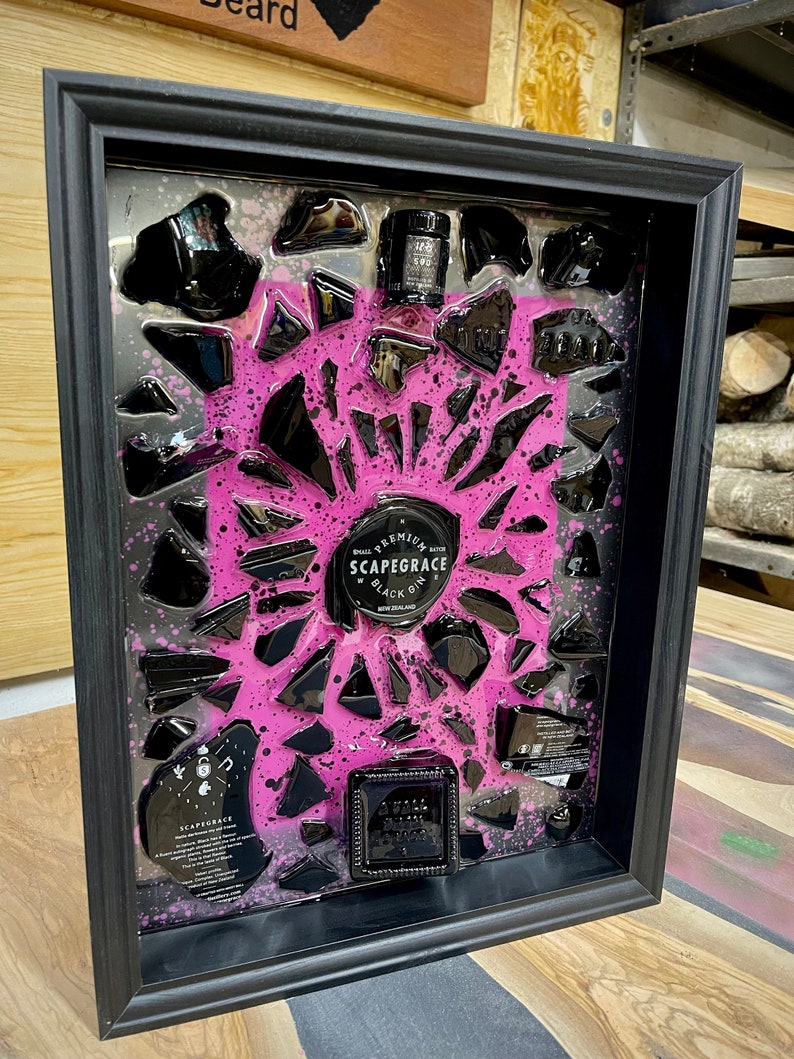 May include: A framed artwork featuring a black and pink design with broken glass pieces. The artwork includes a bottle of "Scapegrace Black Gin" and a label that reads "Small Batch Premium New Zealand Gin".