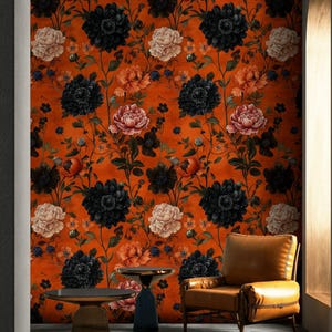 以下が含まれることがあります： オレンジ色の背景に黒と白の花が咲いた花柄の壁紙のあるリビングルームのインテリア。壁紙の前に茶色の革張りのアームチェアが置かれ、円形のジュート製のラグとサイドテーブルが2つある。