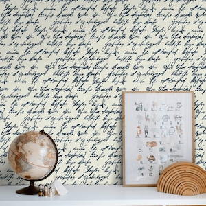 Może przedstawiać: Pokój z kremową ścianą pokrytą ciemnoniebieskim kursywą. Globus, oprawione dzieła sztuki i drewniane zabawki stoją na białej półce nad wiklinowymi koszami. Grafika zawiera kolorowe ilustracje.