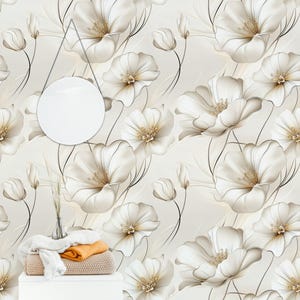 May include: A floral wallpaper design featuring large, cream-colored flowers with golden centers and delicate black stems. The flowers are set against a soft, off-white background, creating a seamless pattern. A white table holds folded blankets and a vase with decorative grass.