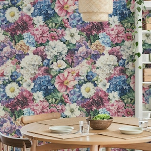 May include: A dining room scene with a floral wallpaper backdrop of pink, purple, blue, and white blooms. A round wooden table is set with plates, placemats, and a bowl of greens. A woven pendant light hangs above.