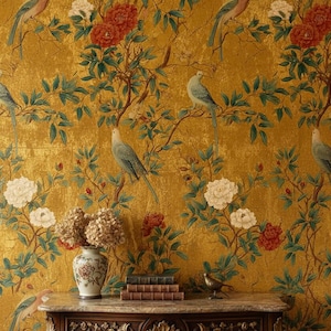 May include: A gold-toned wallpaper with a repeating pattern of birds, flowers, and foliage. The design features birds perched on branches with red and white flowers. A decorative table with a vase of dried flowers and books is in the foreground.