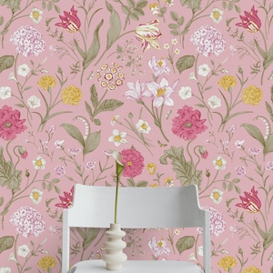Pode incluir: Um design de papel de parede floral rosa com uma variedade de flores em tons de rosa, amarelo e branco, com folhas e caules verdes. Uma cadeira branca e um pequeno vaso branco com uma única flor estão em primeiro plano.