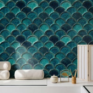 May include: A wall covered in teal and dark blue fish scale tiles with a glossy finish. The tiles feature a repeating scalloped pattern with varying shades of blue and green. The wall is positioned behind a white surface with white cushions.