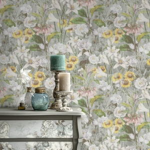 Könnte beinhalten: Eine graue Kommode mit floralem Design, gekrönt von Kerzen und Glasflaschen. Der Hintergrund ist eine Blumentapete mit weißen, gelben und rosa Blumen. Die Kommode hat eine Vintage-Ästhetik.
