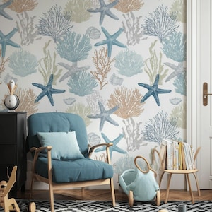 May include: A room with a marine theme, featuring wallpaper with blue starfish and coral patterns. A blue armchair with a matching pillow sits on a black and white patterned rug. Wooden furniture and a toy car complete the scene.