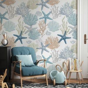 Op de afbeelding: Een kamer met een witte muur bedekt met een herhalend patroon van blauwe zeesterren, koraal en zeewier. Een blauwe fauteuil met een bijpassend kussen staat voor de muur. Een zwart-wit patroon tapijt bedekt de vloer.