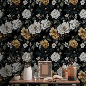 May include: Floral wallpaper featuring a repeating pattern of white and yellow roses against a black background. The image also shows a desk with a vase of flowers, a picture frame, and other decorative items.