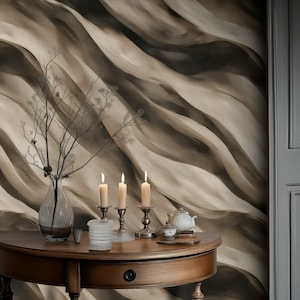 May include: A wooden, half-moon table with a drawer holds a vase with branches, three lit candles in silver holders, and a tea set. The background is a wall with a flowing, abstract pattern in shades of brown and beige.