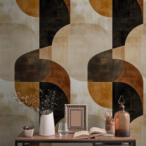 Può includere: Una stanza con carta da parati geometrica nei toni del marrone, beige e nero. Una scrivania in legno con cornice in metallo nero espone un vaso bianco con fiori secchi, una cornice, un bicchiere d'acqua e una bottiglia marrone.