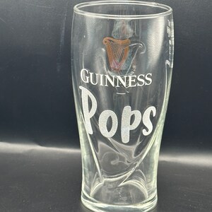 May include: A clear glass pint glass with the Guinness logo and the word "Pops" etched on the side.