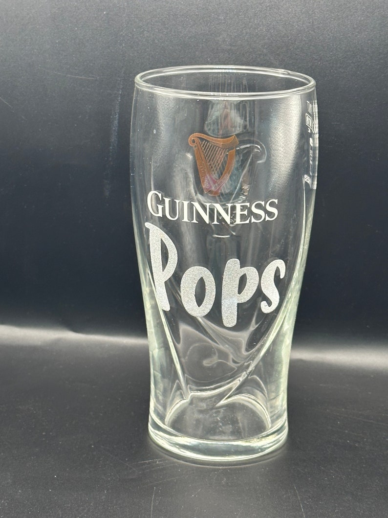 May include: A clear glass pint glass with the Guinness logo and the word "Pops" etched on the side.