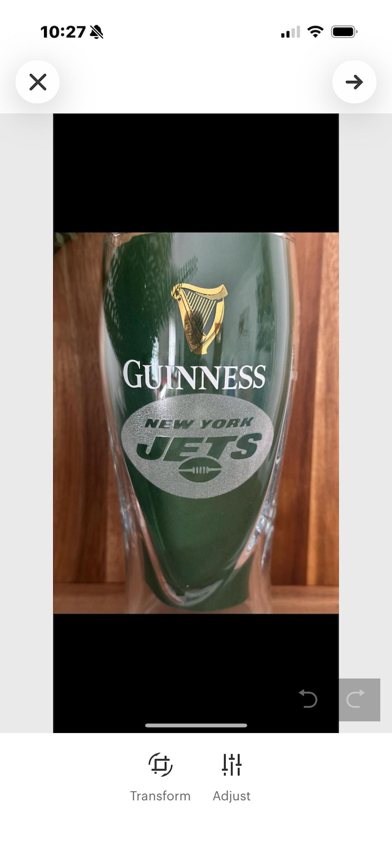 May include: A green Guinness pint glass with the New York Jets logo. The glass features the Guinness logo in gold and the Jets logo in white and green. The glass is on a wooden surface.