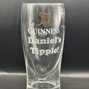 May include: A clear glass pint glass with a Guinness logo and the text "Daniel's Tipple!" etched on the side.