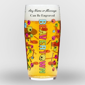 Op de afbeelding: Een hoge, heldere glazen bierpul met een kleurrijk ontwerp met schedels, botten en de woorden "BEAVERTOWN". De tekst "Any Name or Message Can Be Engraved" staat bovenaan de pul.