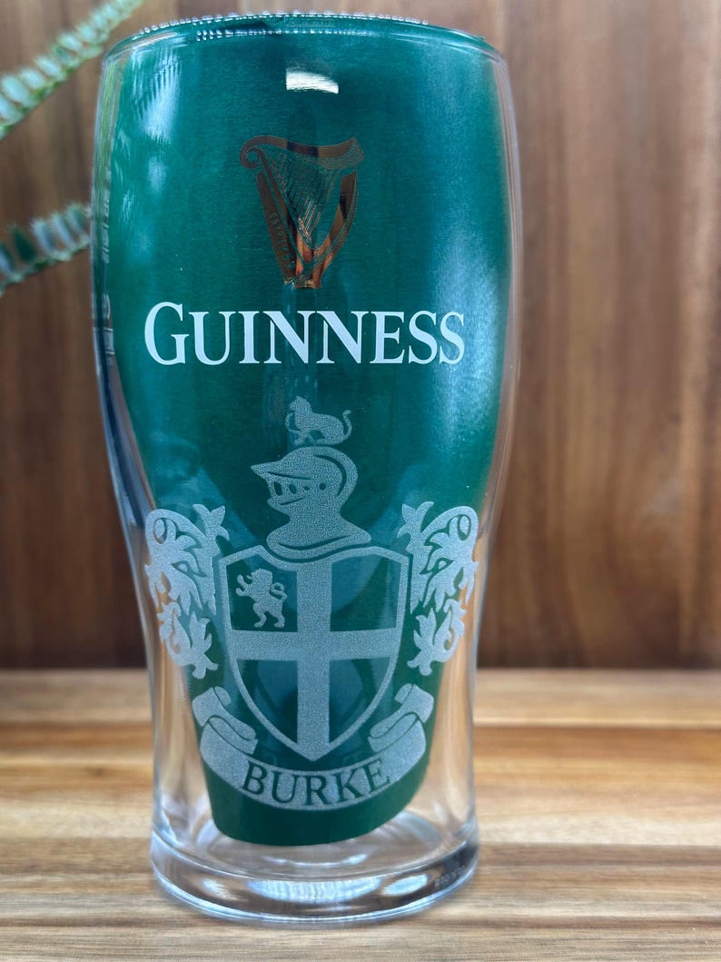 May include: A clear pint glass with the Guinness logo and the name "Burke" etched on it. The glass has a green background and a classic design, perfect for enjoying a pint of stout.