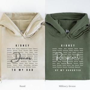 May include: Two hooded sweatshirts, one sand-colored and one military green. Each features the word "KIDNEY" and a list of related words. The sand-colored hoodie says "TO MY DAD" and the green one says "OF MY DAUGHTER".