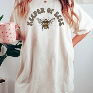 A ivory-colored t-shirt featuring a honey bee graphic and that reads Keep of bees in retro font. A Perfect Beekeeper Shirt Bee T Shirt Honey Bee T-shirt Bee Keeper Tshirt Beekeeping Shirt Vintage Bee Graphic Tee Comfort Colors Gift For Bee Lovers!