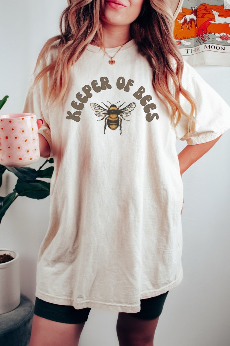 A ivory-colored t-shirt featuring a honey bee graphic and that reads Keep of bees in retro font. A Perfect Beekeeper Shirt Bee T Shirt Honey Bee T-shirt Bee Keeper Tshirt Beekeeping Shirt Vintage Bee Graphic Tee Comfort Colors Gift For Bee Lovers!
