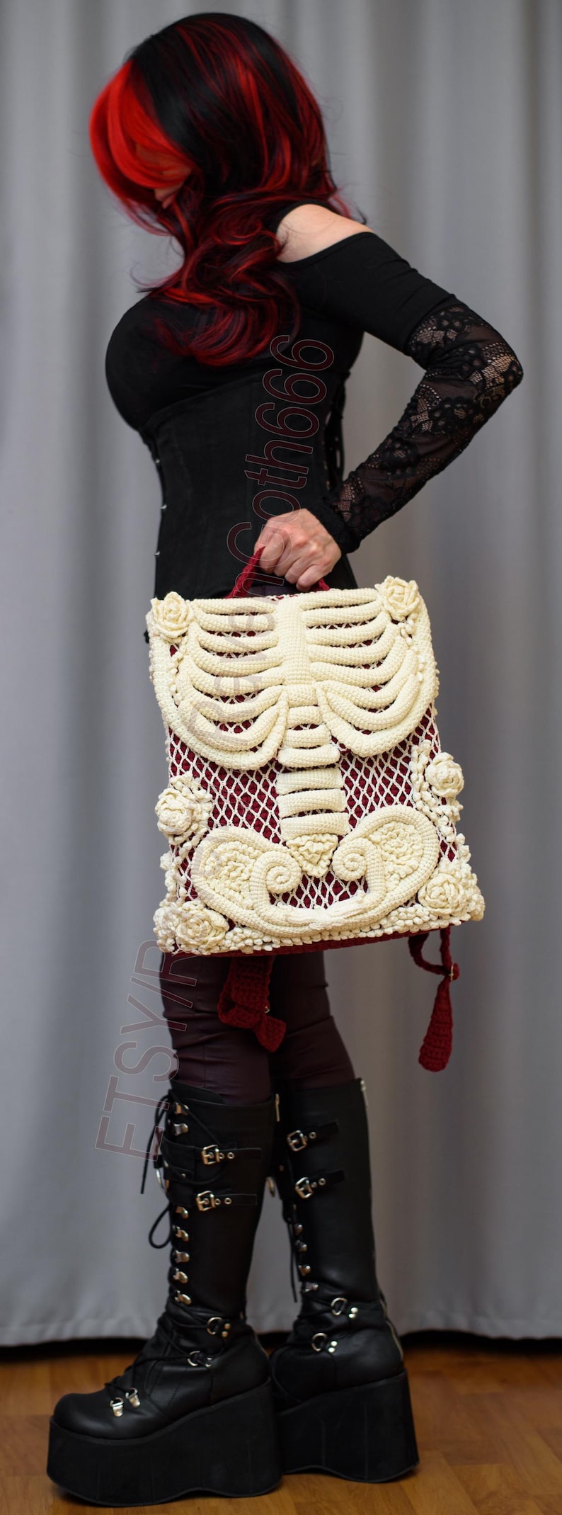 K&ouml;nnte beinhalten: Eine einzigartige Handtasche mit cremefarbenem H&auml;kelskelett-Design auf burgunderrotem Hintergrund. Die Tasche hat cremefarbene Rosen und einen roten Griff. Die Person tr&auml;gt schwarze Plateau-Stiefel.