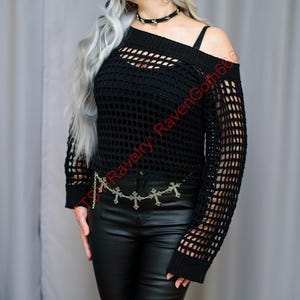 Può includere: Top nero all'uncinetto con spalle scoperte e maniche lunghe. Il top ha un design a rete ed è abbinato a pantaloni di pelle neri e una cintura a catena argentata con croci. Il testo "TS Ravelry RavenGoth66" è visibile.