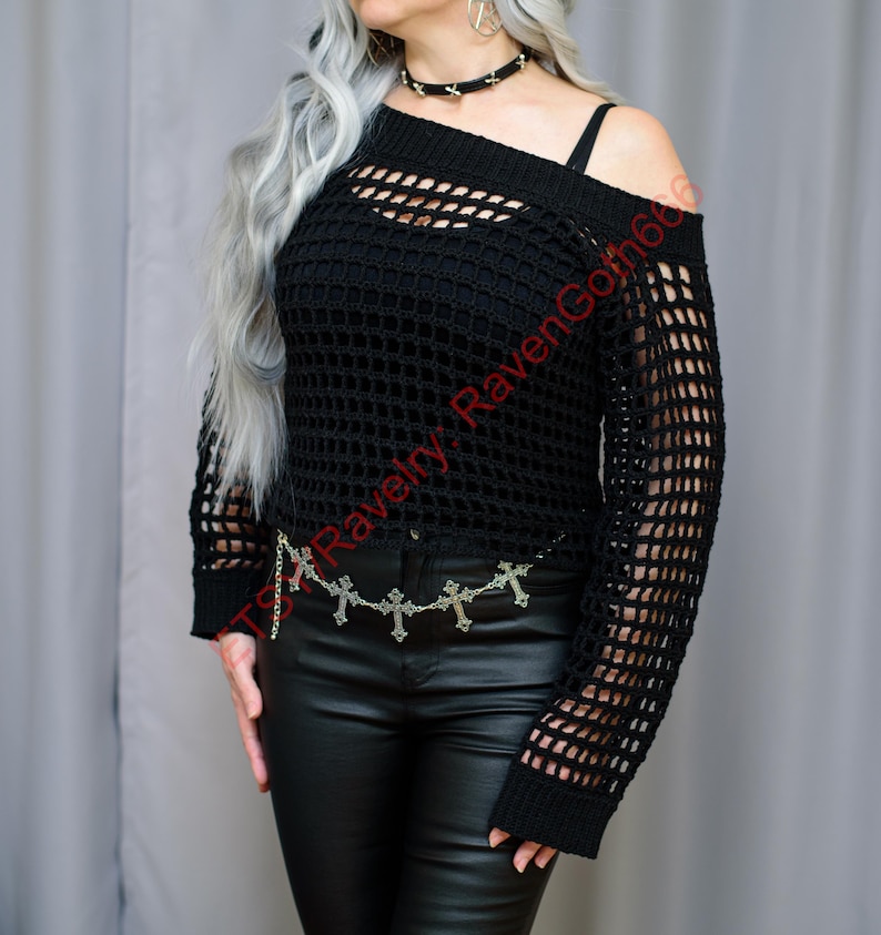 Op de afbeelding: Zwarte gehaakte off-the-shoulder top met lange mouwen. De top heeft een mesh design en wordt gecombineerd met een zwarte leren broek en een zilveren kruisjeskettingriem. De tekst "TS Ravelry RavenGoth66" is zichtbaar.