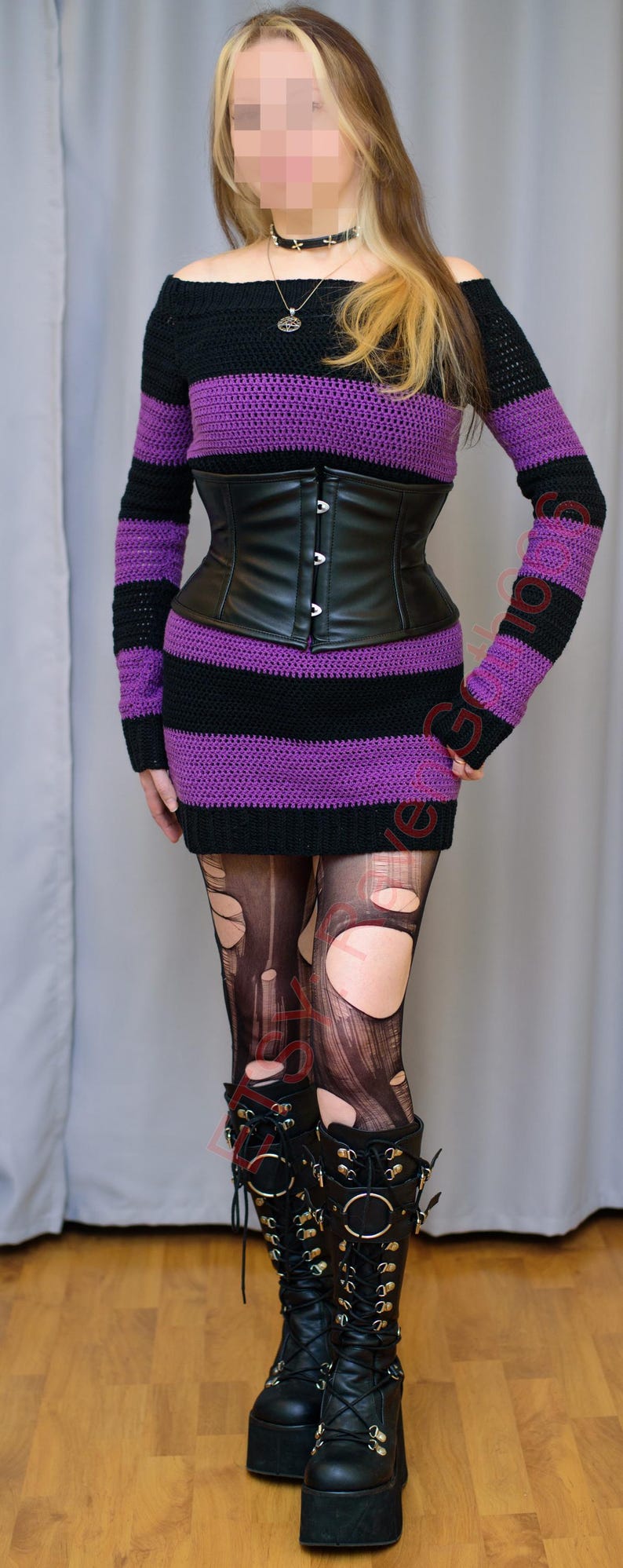 Pode incluir: Um vestido preto e roxo listrado com ombros de fora e um espartilho de couro preto. O traje inclui meias pretas rasgadas e botas de plataforma pretas. Um pingente de prata pende de um choker preto.