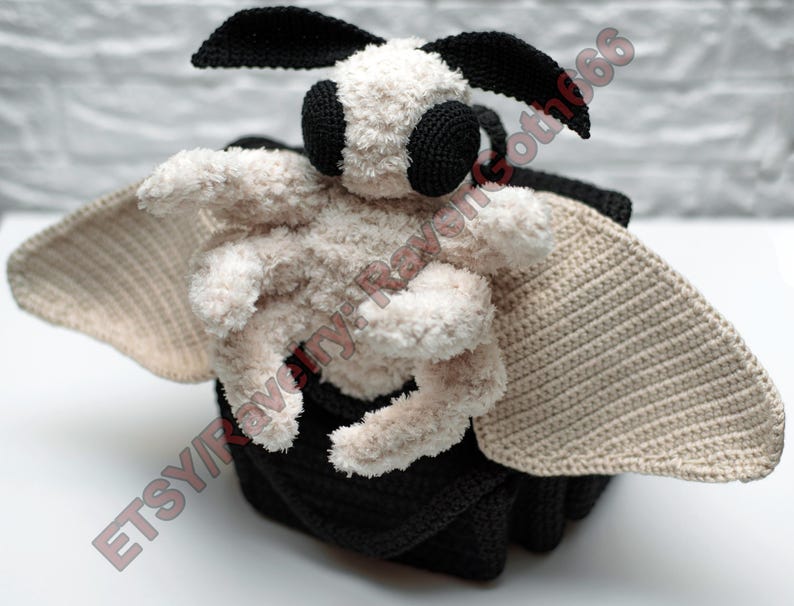 May include: A handcrafted crochet moth toy. The moth features a soft, cream-coloured body, large beige wings, and black details on the eyes and antennae. It rests on a black base. The Etsy shop name is visible in the image.