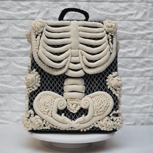 May include: A black backpack with a cream-coloured crocheted skeleton design. The backpack has a black handle and cream-coloured floral accents. The skeleton design is the main feature on the front of the bag.