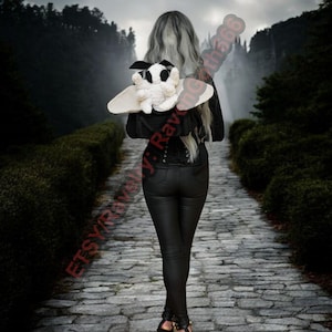 May include: A person walks along a stone path, holding a black and white plush moth with cream wings. The moth has black spots and a black bow. The person wears black trousers and a black jacket.