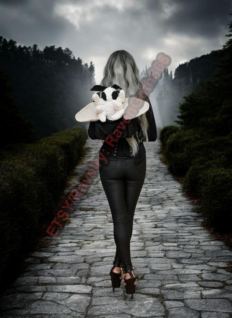 May include: A person walks along a stone path, holding a black and white plush moth with cream wings. The moth has black spots and a black bow. The person wears black trousers and a black jacket.