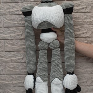 May include: A crocheted robot toy with a white body, gray arms and legs, and black accents. The robot has large blue eyes and a friendly expression.