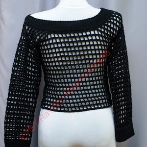 Op de afbeelding: Zwarte gehaakte top met een brede halslijn en lange mouwen. Het open geweven ontwerp cre&euml;ert een netachtig uiterlijk. De top wordt getoond op een witte mannequin, die de vorm en textuur van het kledingstuk laat zien. Een stijlvolle en unieke toevoeging aan elke garderobe.