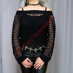 Op de afbeelding: Zwarte off-the-shoulder gehaakte trui met lange mouwen. De trui heeft een mesh-ontwerp en wordt gecombineerd met een zwarte leren broek en een zilveren kruiskettingriem. De top wordt over een zwarte camisole gedragen.