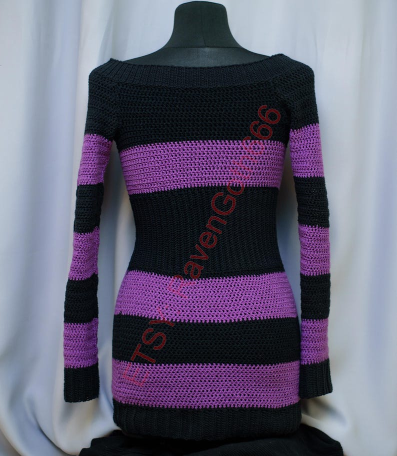 Pode incluir: Vestido de croch&ecirc; listrado preto e roxo com mangas compridas. O vestido apresenta um decote canoa e listras horizontais em preto e roxo. O vestido &eacute; exibido em um manequim preto.