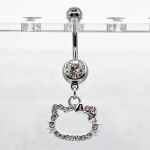 Puede incluir: Un piercing para el ombligo de color plateado con un dije de Hello Kitty colgante. El dije y los dos acentos redondos del anillo están incrustados con cristales transparentes. El anillo está suspendido de una pantalla de plástico transparente.