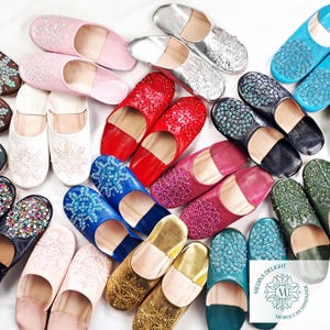 May include: Assortment of colorful Moroccan leather slippers with intricate beaded designs. The slippers are handmade and feature a variety of colors, including pink, blue, green, gold, and red.