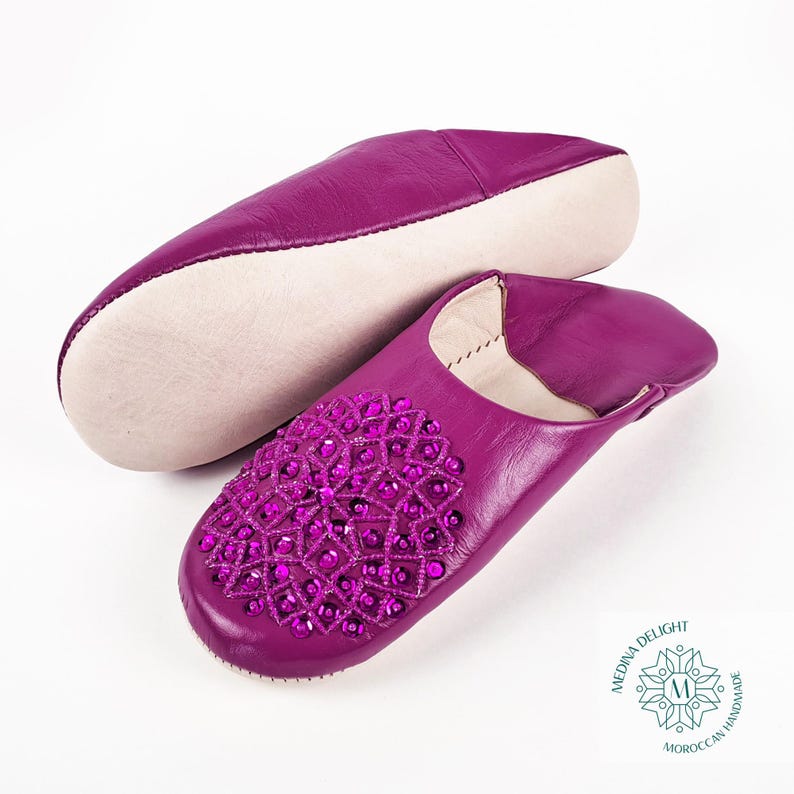 May include: A pair of purple leather slippers with a jeweled design. The slippers are handmade in Morocco.