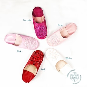 May include: Five pairs of leather slippers with jeweled embellishments in various colors, including fuchsia, rose, pink, red, and white. The slippers are handmade and feature a Moroccan design.