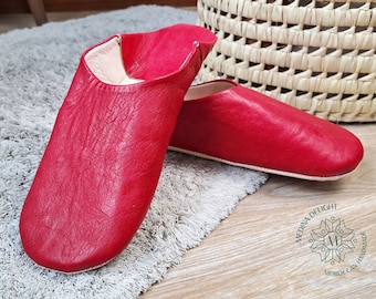 May include: A pair of red leather slippers with a textured surface. The slippers are on a gray rug.