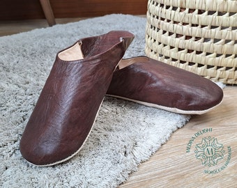 Puede incluir: Un par de zapatillas de cuero marrón con costuras blancas. Las zapatillas están sobre una alfombra gris claro.