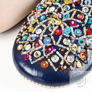 May include: Close-up of a navy blue leather slipper with colorful sequins and beads. The slipper has a geometric pattern and is decorated with a variety of colors, including gold, silver, red, green, blue, and purple.