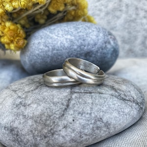 Peut inclure: Deux anneaux en argent avec un design arrondi et légèrement incurvé. Les anneaux sont empilés l'un sur l'autre et reposent sur une pierre grise.